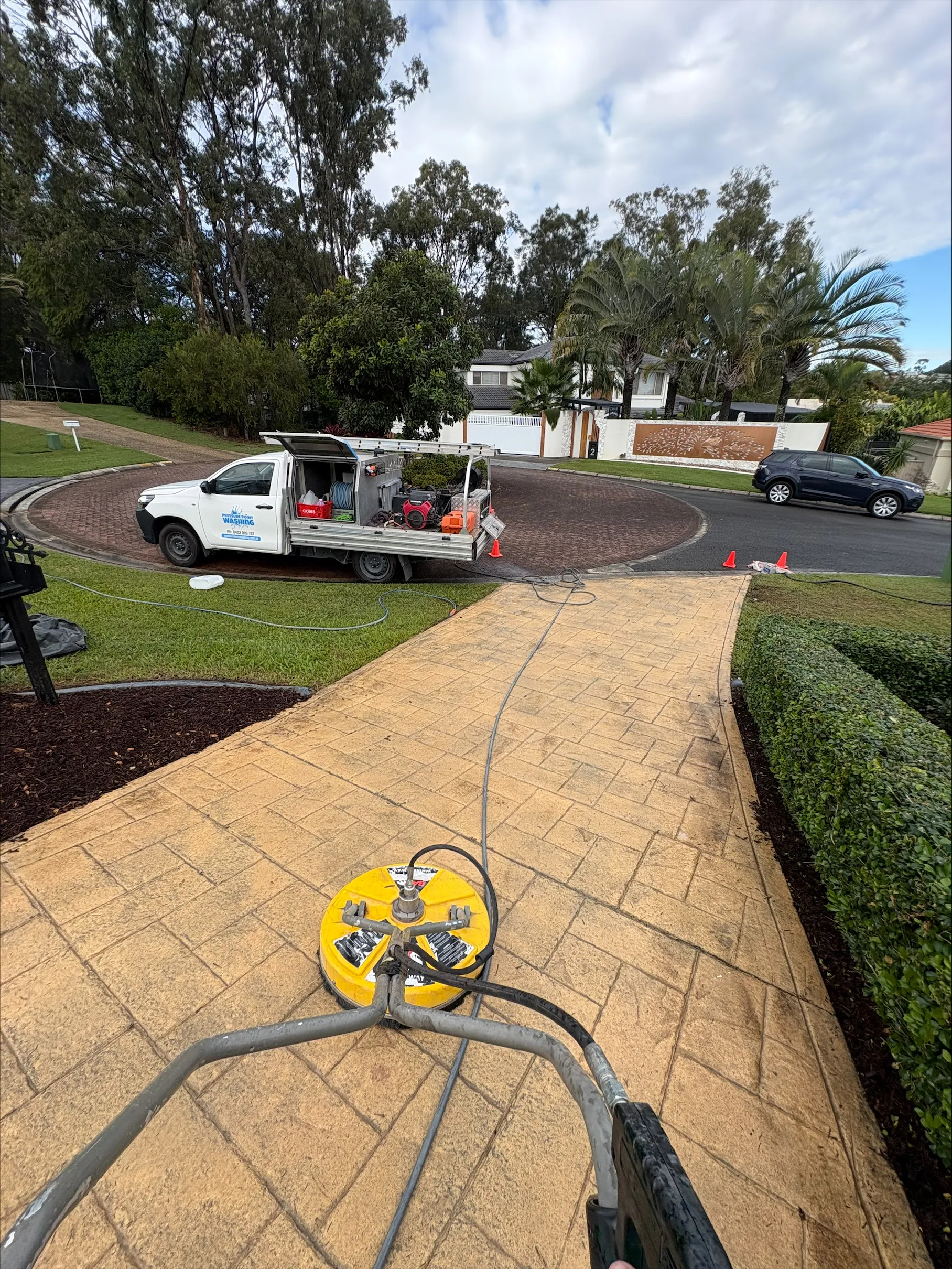 Driveway pressure washing in progress with professional surface cleaner and branded ute